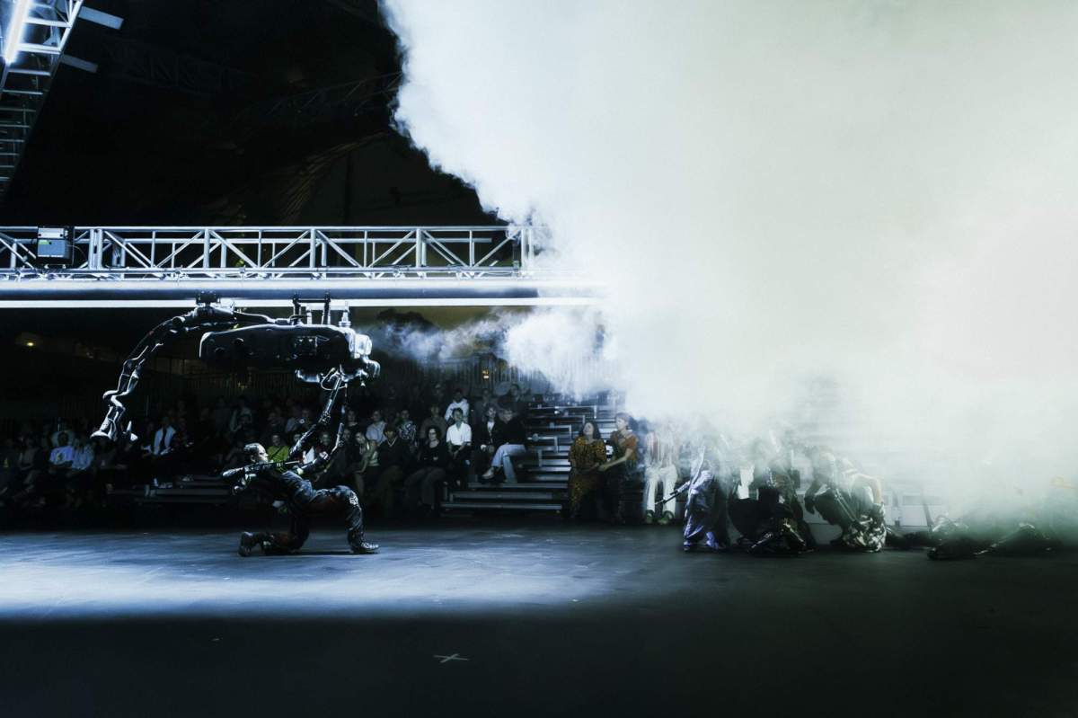 U>N>I>T>E>D Chunky Move, a dark stage with dramatic smoke effects and white lighting showing a female performer with robotic metallic costuming moving across the stage under a scaffolding set piece.