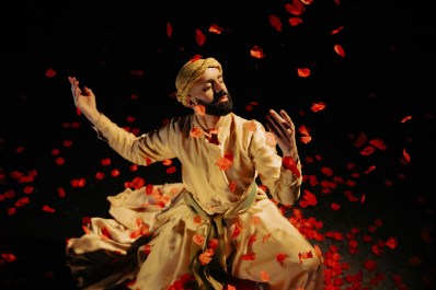 Songs of the Bulbul Aakash Odedra: a young male dancer in a white turban and robe photographed spinning with his eyes closed under a shower of red rose petals that are descending on him from above.