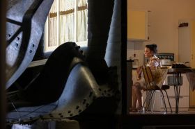 Daniela Farinacci on the set of MTC's 2026 production, West Gate. The actor, playing a grieving widow, sits in a reproduction of a 1970's kitchen surrounded by the wreckage of the collapsed West Gate Bridge.