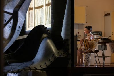 Daniela Farinacci on the set of MTC's 2026 production, West Gate. The actor, playing a grieving widow, sits in a reproduction of a 1970's kitchen surrounded by the wreckage of the collapsed West Gate Bridge.