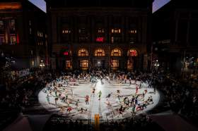CERCLES, STRUT Dance, Perth Festival: a photo of approximately 150 people under a spotlight on a large circular outdoor stage dancing in colourful clothing at night, against the night sky.