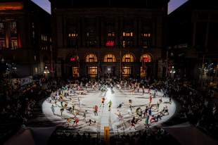 CERCLES, STRUT Dance, Perth Festival: a photo of approximately 150 people under a spotlight on a large circular outdoor stage dancing in colourful clothing at night, against the night sky.
