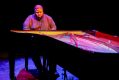 Tyshawn Sorey: Alone at Adelaide Festival 2026. A tall, solidly built African American man with closely cropped hair and a matching beard, and wearing a black business shirt, sits at an open-topped piano.