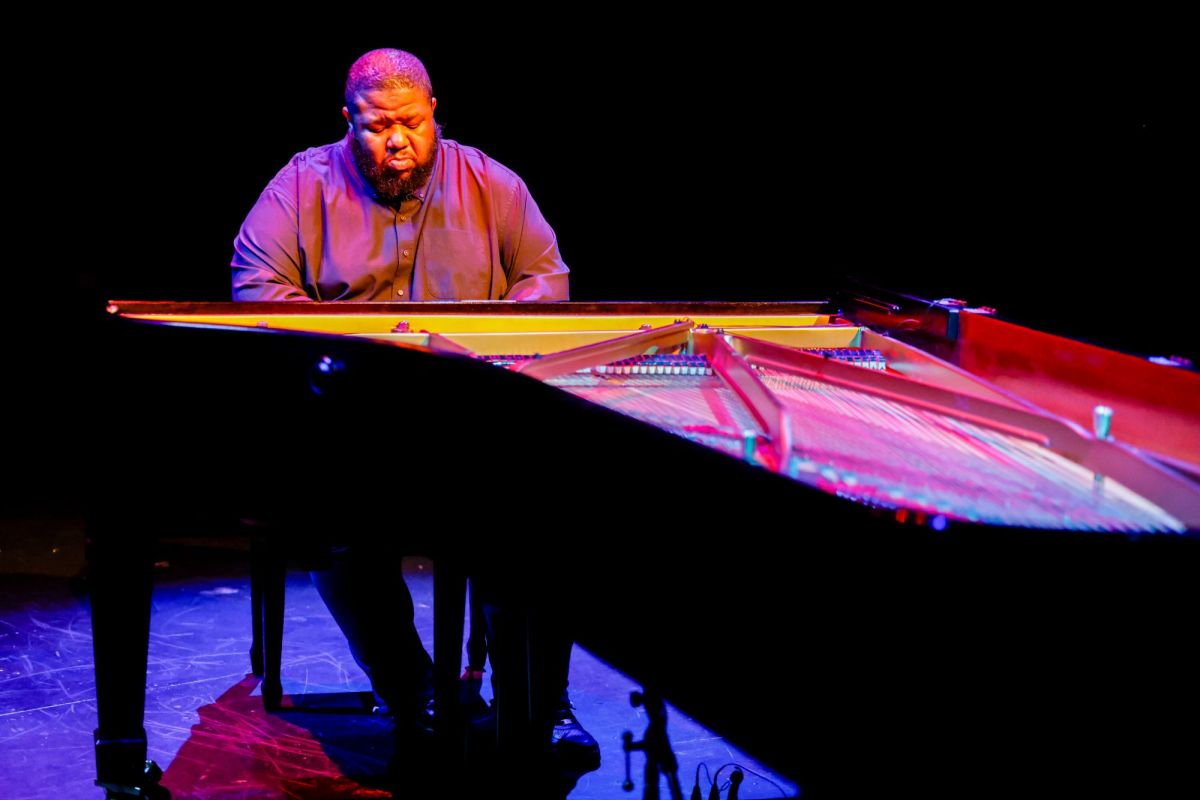 Tyshawn Sorey: Alone at Adelaide Festival 2026. A tall, solidly built African American man with closely cropped hair and a matching beard, and wearing a black business shirt, sits at an open-topped piano.