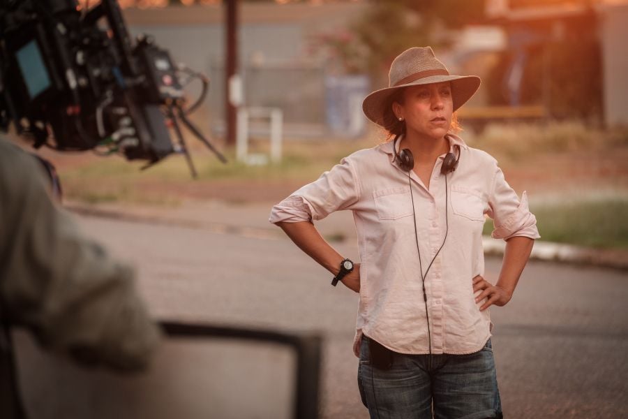 Rachel Perkins, Screen Australia's newly appointed Director of First Nations Strategy. An Aboriginal woman wearing jeans and a collared shirt with the sleeves pushed uo, stands with her hands on her hips. She is also wearing a broad brimmed hat, and headphones around her neck. A camera operator is visible on the left hand side of the photo. arts sector appointments