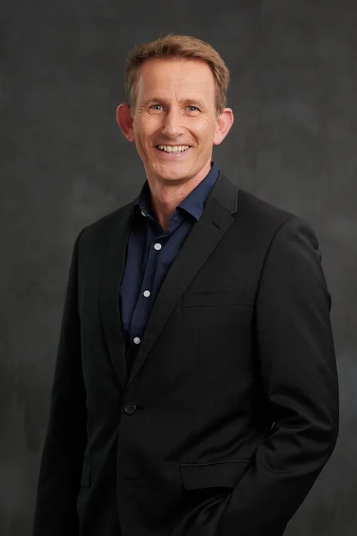Rick Heath, the new Executive Director of The Chamber of Arts and Culture WA. A fair skinned man with short brown hair smiles at the camera. He is wearing a black suit jacket and a dark blue collared shirt.
