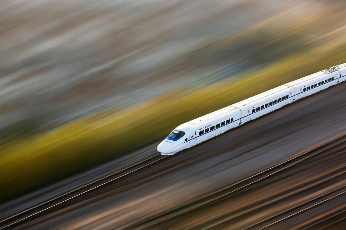 A high speed train passing through a blurred landscape; the photograph is taken from a high angle so that the train is crossing the image diagonally, from the upper right side of the frame towards the bottom left. arts sector appointments