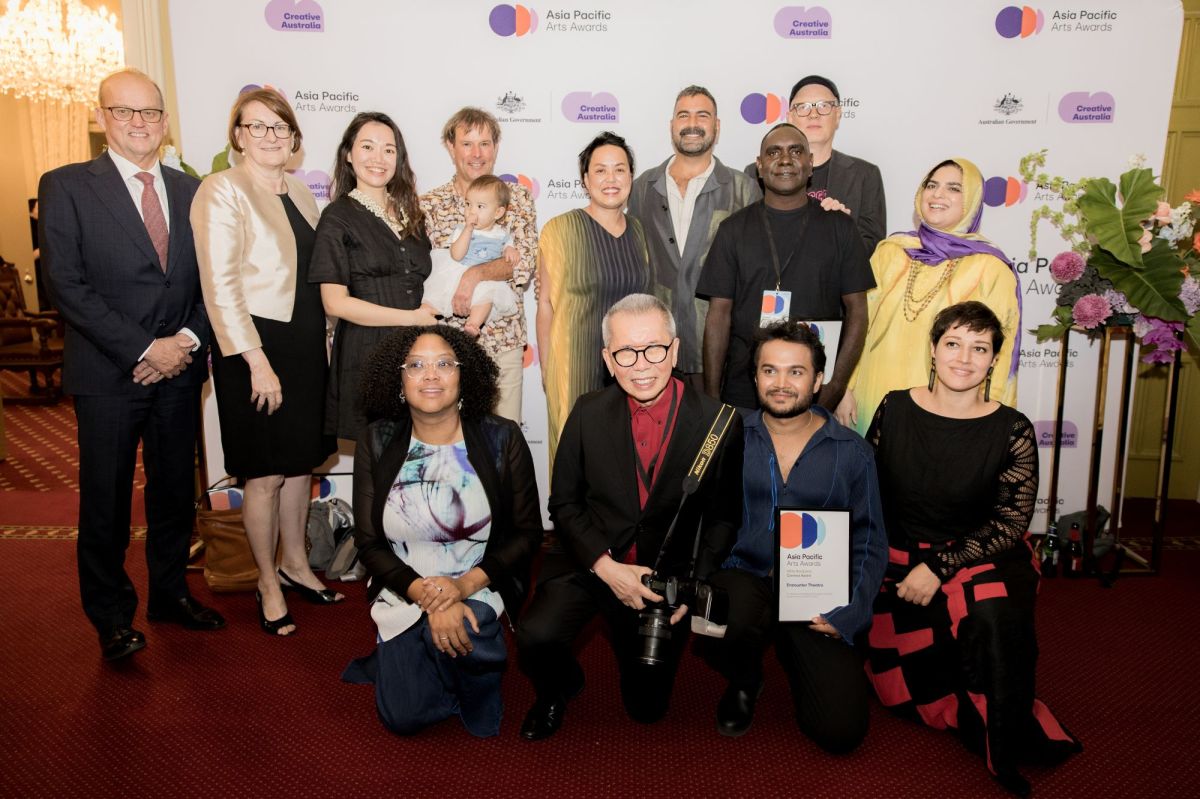 Asia Pacific Arts Awards 2026 recipients at Government House Ballroom, WA. A group of 13 adults and a baby, some standing and others kneeling; the group is culturally and gender diverse, and of various ages.