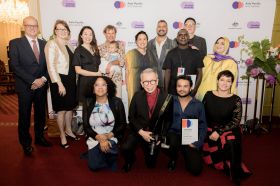 Asia Pacific Arts Awards 2026 recipients at Government House Ballroom, WA. A group of 13 adults and a baby, some standing and others kneeling; the group is culturally and gender diverse, and of various ages.