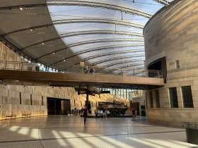 Partial view of the Australian War Memorial’s Anzac Atrium space., a light-filled, glass ceiling atrium space with a walkway bridge dividing the space horizontally.