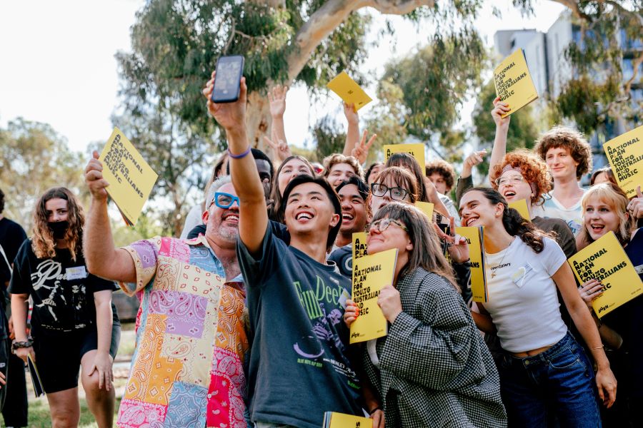 A group of young people posing for a selfie and holding copies of A National Plan for Young Australians and Music, which has a bright yellow cover and the title emblazoned in large black capital letters. 10-year plan for young Australians and music