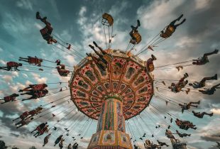 A colourful fairground ride showing people swinging around the ride's central support structure in flying seats tethered by chains, and pictured against a dramatic sky. arts sector appointments