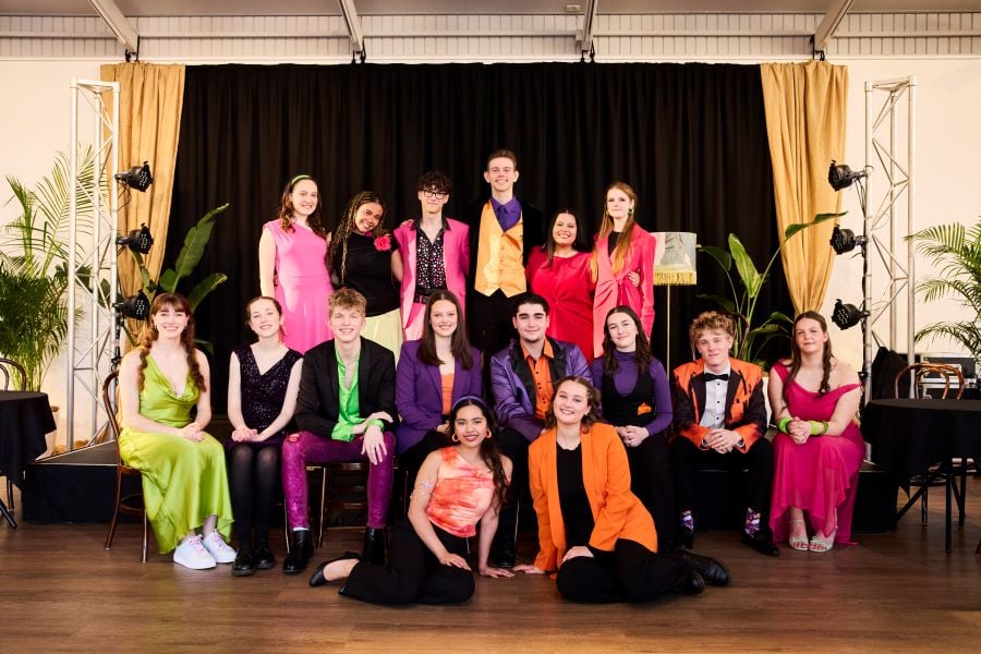 Adelaide Cabaret Festival's Class of Cabaret 2025. Seventeen teenagers in Years 10 and 11 sit and stand at the edge of a low stage. All 17 are dressed in brightly coloured clothes: glittering purple trousers, a purple shirt with an orange vest in one instance, a bright green dress, a bright pink dress etc.