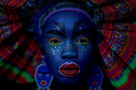 Atong Atem, Ego 2 (2019) from the Ego series (2019). A striking self-portrait of the Melbourne-based South Sudanese artist, in which her skin is painted blue, rows of small gold stars decorate her cheeks, and her lips are painted bright red.Her colourful headdress frame the image and also forms its backdrop.
