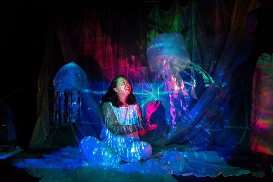 Luminous Productions' Gunamidirra, an immersive work for families exploring the underwater life of Saltwater Country, will have its world premiere at Darwin Festival 2026. A performer dressed in white sits cross-legged on stage, surrounded by giant floating jellyfish and bright lights.