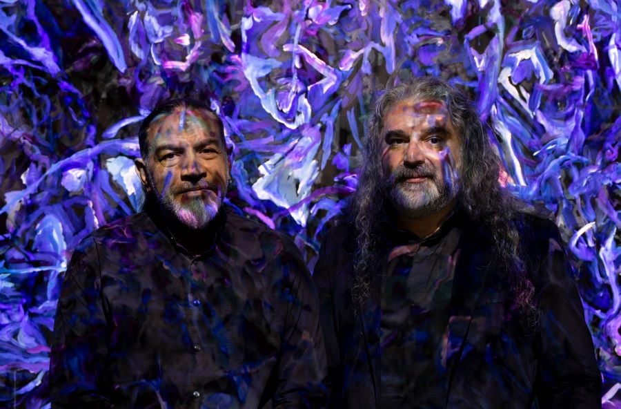 Artist Khaled Sabsabi and curator Michael Dagostino standing in front of Sabsabi's 2026 Venice Biennale work, conference of one’s self, and lit by one of the work's projectors.