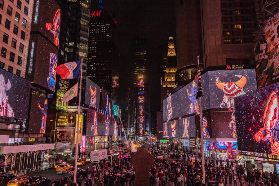 Native American artist Cannupa Hanska Luger's work Midéegaadi projected in New York City's Times Square; the work comes to Fed Square for RISING's opening weekend. A dozen digital billboards project an image of a person in Native American dress featuring a horned headdress; the cityscape stretches out in the background and crowds mingle on the street below.