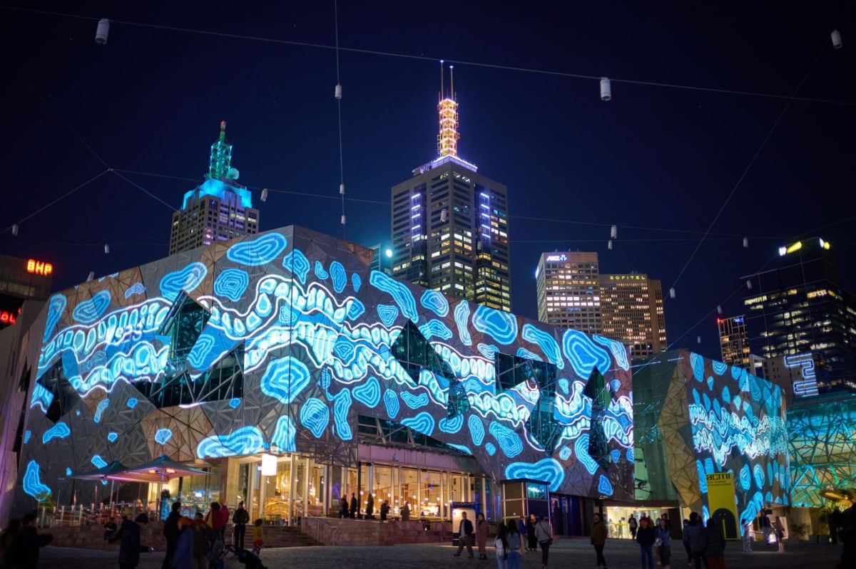 In partnership with Fed Square, the Square transforms into an open-air canvas for the opening weekend of RISING. Vivid projections in blue light adorn the buildings of Melbourne's Fed Square,; towering CBD rise behind them towards the night sky.