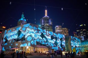 In partnership with Fed Square, the Square transforms into an open-air canvas for the opening weekend of RISING. Vivid projections in blue light adorn the buildings of Melbourne's Fed Square,; towering CBD rise behind them towards the night sky.