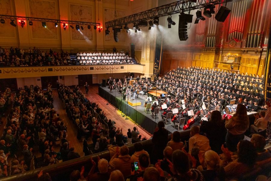 Royal Melbourne Philharmonic Orchestra and Choir in concert. The photograph, taken from the balcony in Melbourne Town Hall, shows the orchestra and choir arrayed on stage before the Town Hall's pipe organ. Additional choir members, wearing white, are seated in the opposite balcony; audience memebrs are visible in both balconies and seated in rows on the floor below. creative industries 