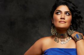 Tara Tiba – Omid (Hope) at Adelaide Cabaret Festival 2026. Tiba, an Iranian-Australian performer, wears a sleeveless dress of vivid blue and stands with her left hand raised and resting on one shoulder. She wears a heavy bracelet, large earrings and a striking necklace, and looks upwards to her right.