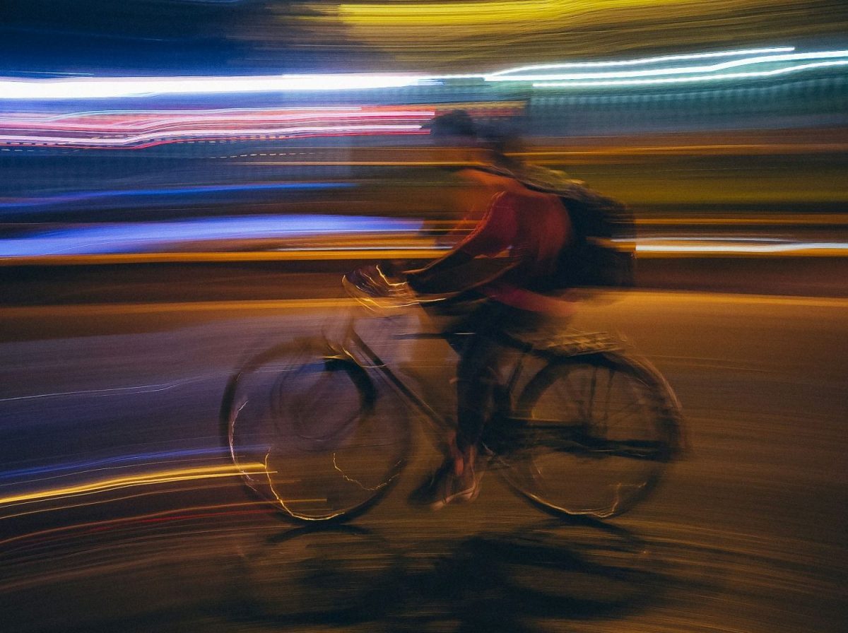 A cyclist rides through a city at night; their movement and the rivers of live behind them are blurred, suggesting rapid movement. arts sector appointments