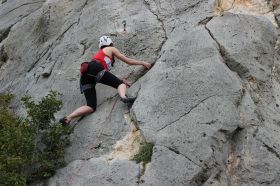 A female rock climber, photographed from below as she ascends a sheer rock face. arts sector appointments