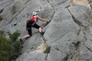 A female rock climber, photographed from below as she ascends a sheer rock face. arts sector appointments