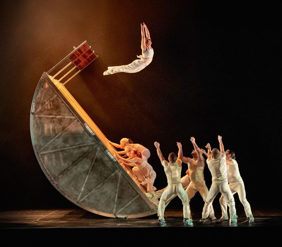 ESCAPE by DIAVOLO | Architecture in Motion has been programmed at Brisbane Festival 2026. A group of circus artists dressed in white stand poised to catch another acrobat who flies towards them, flung from a large structure manipulated by others of their troupe.