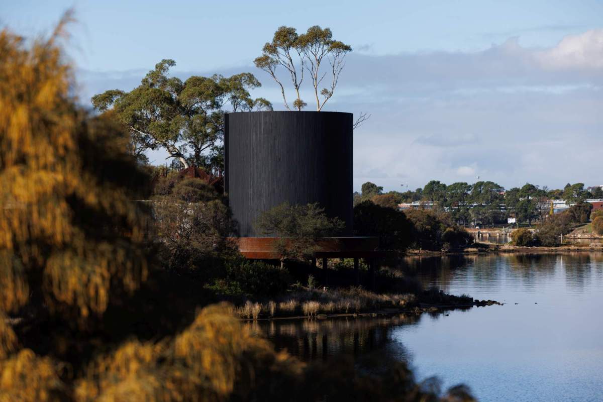 In Absence Mona Yhonnie Scarce: a photo of a large ciccular ashen-coloured wooden tower installed amongst trees on the edge of a river which is Berriedale Bay in Nipaluna/ Hobart.