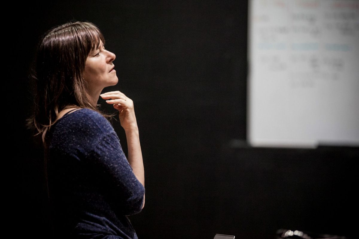 Lucy Guerin. The choreographer stands thoughtfully, her hand under her chin, gazing into the distance.