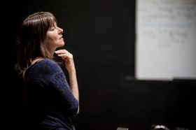 Lucy Guerin. The choreographer stands thoughtfully, her hand under her chin, gazing into the distance.