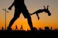 A barefoot youth is caught mid-summersault, silhouetted against the setting sun; other people walk past him and behind him. arts sector appointments