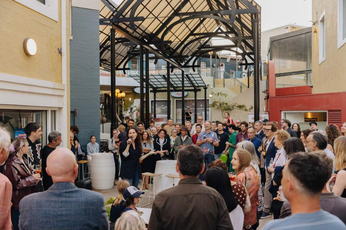 new arts precinct: a photogrpah of a small outdoor piazza space packed with people listening to an opening address to an arts event.