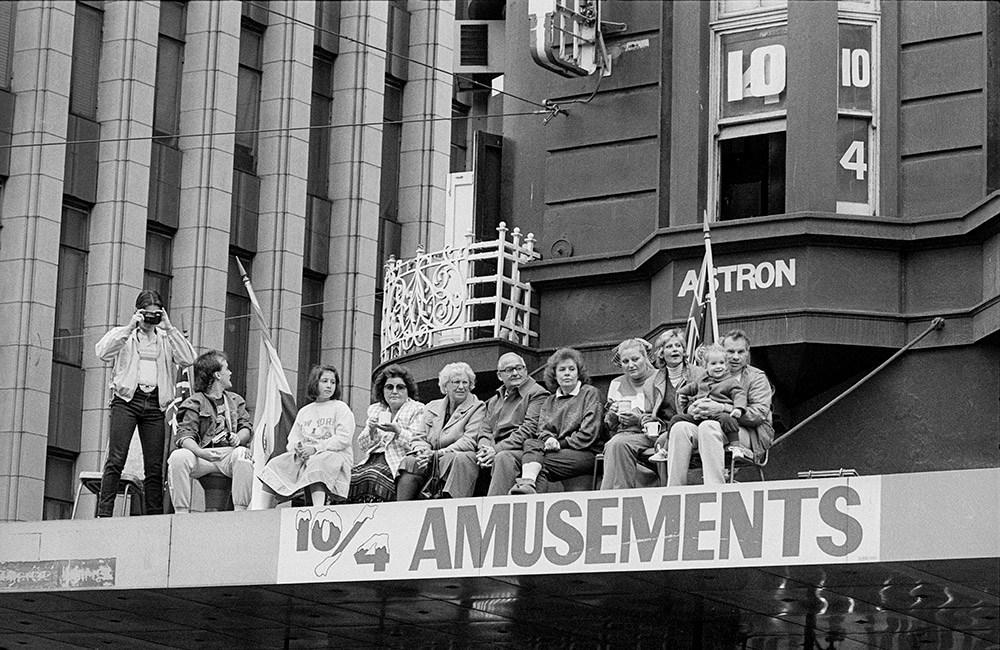 Andrew Chapman, People sitting on top of a shop awning on Swanston Street watching the Moomba Parade, corner of Swanston and Little Collins Streets, March 1987. Gelatin silver print, City of Melbourne Art and Heritage Collection. Courtesy: Andrew Chapman Photography.