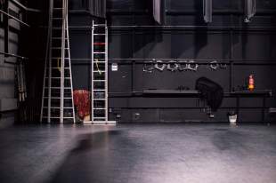 performing arts cost increases: a photo of a theatre's empty stage showing a ladder against its back wall and some equipment items at the back of the stage.