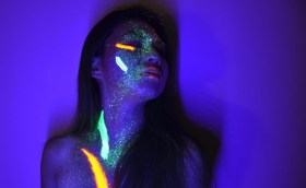 OzAsia 2018: a photo of a purple neon-lit studio showing the shadowed face of female Asian person whose face is covered in strips of brightly coloured neon lighting effects.