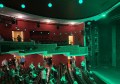 theatre audience etiquette: a photo of the inside of a theatre showing the seating bank and part of the stage. The lighting from the stage is casting green light over the audience.