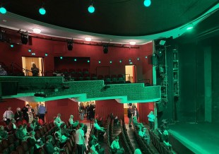 theatre audience etiquette: a photo of the inside of a theatre showing the seating bank and part of the stage. The lighting from the stage is casting green light over the audience.